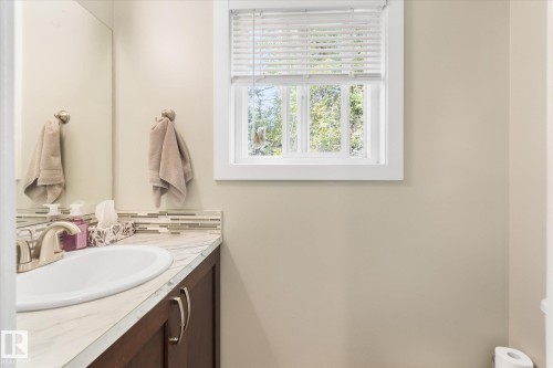 Vanity with an integrated sink, polished chrome faucet, wood-finish cabinetry, and a full-width mirror - 16012 98 Avenue Nw, Edmonton, AB 