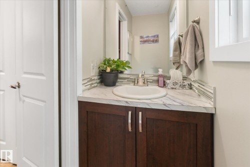 Wood-finish vanity with dual doors, undermount sink, stone-look countertop, and a tiled backsplash - 16012 98 Avenue Nw, Edmonton, AB 