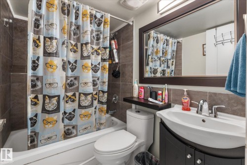 Full bathroom featuring a white porcelain tub, a dark wood-finish vanity with a white basin sink, a frameless mirror, and neutral-toned wall tiling - 16012 98 Avenue Nw, Edmonton, AB 