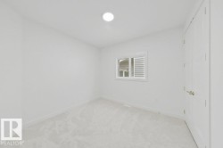 Neutral white wall paint, light-colored carpeting, white trim, a single window, and a white interior door with brushed nickel hardware - 