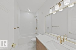 Bathroom featuring a neutral color palette, integrated sink vanity with a wood-finish base, wall-mounted mirror with brass trim, and a bathtub with white subway tile surround and brass fixtures - 