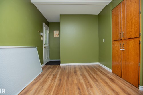 Wood-finish flooring with white trim, a built-in wood cabinet, and a white exterior door - 13032 120 Street Nw, Edmonton, AB 