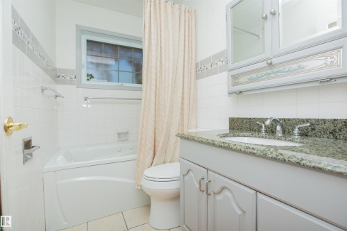 Built-in tub with adjacent toilet, single vanity with integrated sink, stone countertop, and wall-mounted medicine cabinet - 13032 120 Street Nw, Edmonton, AB 
