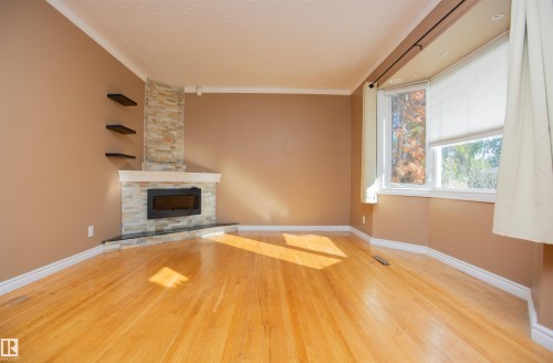 Hardwood flooring, a bay window, a modern fireplace with a stone-clad surround, and decorative floating shelves - 13032 120 Street Nw, Edmonton, AB 
