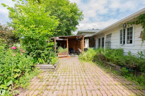 Paved stone walkway with a wooden pergola structure and a white siding exterior with multiple windows - 13032 120 Street Nw, Edmonton, AB 