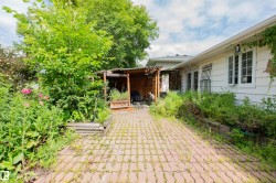 Paved stone walkway with a wooden pergola structure and a white siding exterior with multiple windows - 