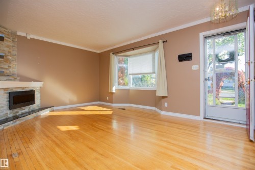 Hardwood flooring, stone-clad fireplace with mantel, bay window, crown molding, and decorative ceiling fixture - 13032 120 Street Nw, Edmonton, AB 
