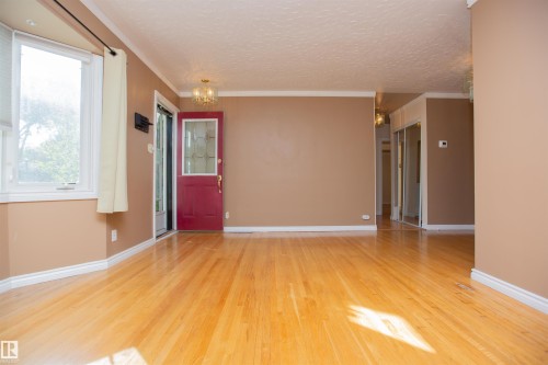 Hardwood flooring throughout, a red entry door with decorative glass, a bay window, and a built-in closet with mirrored sliding doors - 13032 120 Street Nw, Edmonton, AB 