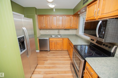 Kitchen featuring wood-finish cabinetry, stainless steel appliances, a double basin sink, light-toned countertops, and wood-finish flooring - 13032 120 Street Nw, Edmonton, AB 
