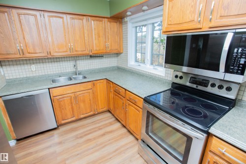 Kitchen featuring wood-finish cabinetry, stainless steel appliances, dual basin sink, and a tiled backsplash - 13032 120 Street Nw, Edmonton, AB 