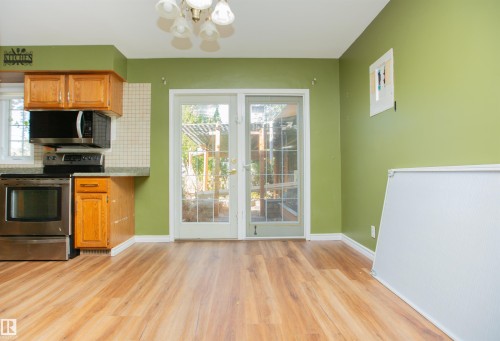 Wood-finish flooring, full light French doors, stainless steel appliances, wood cabinetry, and a tile backsplash - 13032 120 Street Nw, Edmonton, AB 