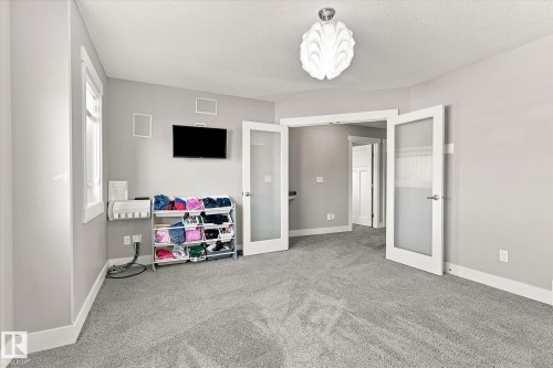 Plush carpet flooring, neutral wall tones, decorative ceiling light fixture, and French doors with frosted panels - 2011 Genesis Lane, Stony Plain, AB 