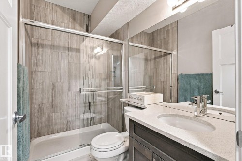 Bathroom featuring a shower with glass enclosure, wood-finish wall tile, a single vanity with stone-finish countertop, and integrated sink - 2011 Genesis Lane, Stony Plain, AB 