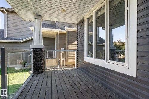 Spacious outdoor deck featuring wood-finish flooring, a glass panel railing, and a stone-accented column - 2011 Genesis Lane, Stony Plain, AB 