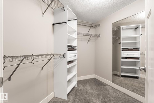Walk-in closet featuring wire shelving, built-in white cabinetry, drawer storage, and full-length mirror - 2011 Genesis Lane, Stony Plain, AB 