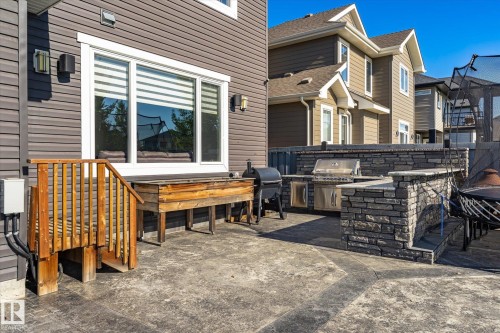 Expansive stamped concrete patio featuring an outdoor kitchen with built-in stainless steel appliances, stone surround, and wood-finish siding - 2011 Genesis Lane, Stony Plain, AB 