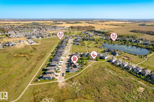Aerial perspective of a residential community with numerous homes, a prominent pond, and expansive green spaces - 2011 Genesis Lane, Stony Plain, AB 