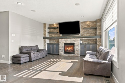 Stone-clad fireplace with built-in cabinetry, wood-finish flooring, recessed lighting, and large windows with blinds - 2011 Genesis Lane, Stony Plain, AB 