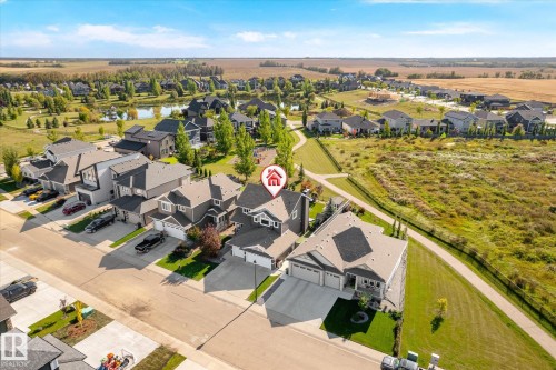 Aerial perspective showcasing a residential neighborhood with landscaped properties, a street, and a nearby pond - 2011 Genesis Lane, Stony Plain, AB 