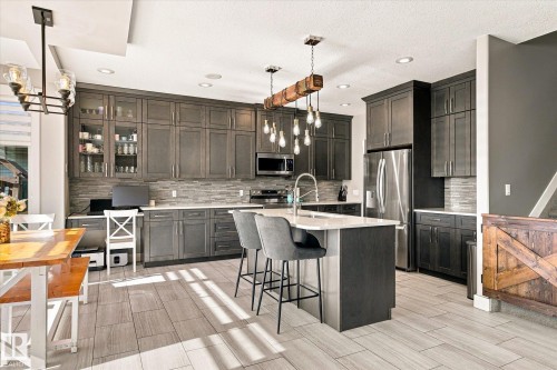 Modern kitchen featuring dark wood-finish cabinetry, stainless steel appliances, a center island with seating, and wood-finish tile flooring - 2011 Genesis Lane, Stony Plain, AB 