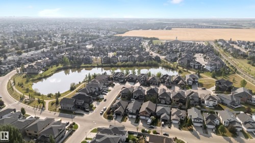 Residential neighborhood featuring a central pond, surrounding homes with diverse architectural styles, and an expansive field in the background - 10621 175A Avenue Nw, Edmonton, AB 