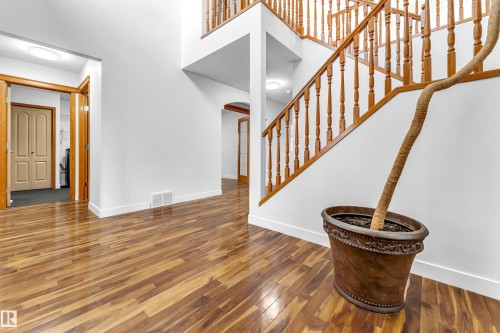Foyer featuring wood-finish flooring, a grand staircase with wood railings, white baseboards, and an arched doorway - 10621 175A Avenue Nw, Edmonton, AB 