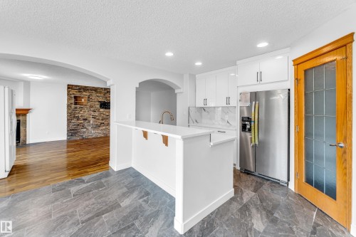 Kitchen featuring white cabinetry, stainless steel refrigerator, white countertops, and a marble-patterned backsplash - 10621 175A Avenue Nw, Edmonton, AB 