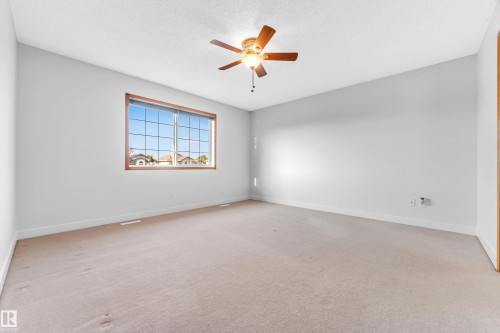 Spacious room featuring neutral wall tones, textured ceiling, a ceiling fan with wood-finish blades, and a large window with a wood-finish frame - 10621 175A Avenue Nw, Edmonton, AB 
