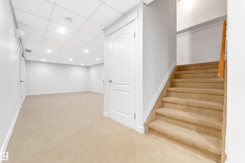 Carpeted staircase with wooden handrail, white walls, and a drop ceiling featuring recessed lighting - 10621 175A Avenue Nw, Edmonton, AB 