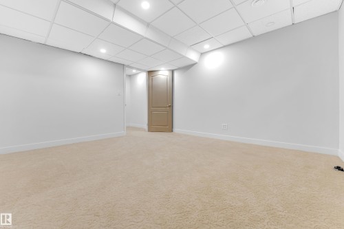 Carpeted room featuring a drop ceiling with recessed lighting, light-toned walls, white baseboards, and a paneled interior door with a lever handle - 10621 175A Avenue Nw, Edmonton, AB 