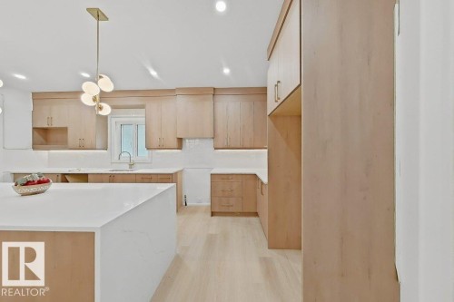 Spacious kitchen featuring light wood-finish cabinetry, bright white countertops, and a modern multi-bulb pendant light fixture - 9216 91 Street Nw, Edmonton, AB - Indoor Photo Showing Kitchen