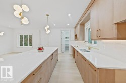 Spacious kitchen featuring a long center island with a light-toned countertop, wood-finish cabinetry with brass hardware, and a double-basin sink with a gold-tone faucet - 