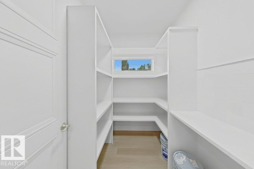Walk-in pantry featuring white shelving, a transom window, and wood-finish flooring - 9216 91 Street Nw, Edmonton, AB - Indoor