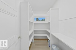 Walk-in pantry featuring white shelving, a transom window, and wood-finish flooring - 