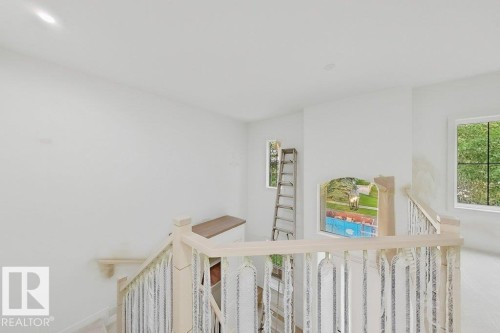 Upper-level landing featuring a light wood banister, white walls, and multiple windows providing natural illumination - 9216 91 Street Nw, Edmonton, AB - Indoor Photo Showing Other Room