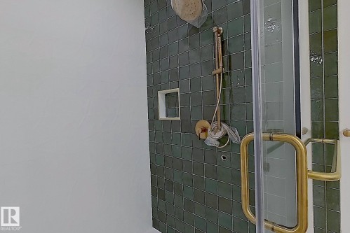 Shower enclosure featuring green square tile, gold-finish shower fixtures, a built-in shower niche, and a clear glass door with a gold-finish handle - 9216 91 Street Nw, Edmonton, AB - 