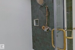 Shower enclosure featuring green square tile, gold-finish shower fixtures, a built-in shower niche, and a clear glass door with a gold-finish handle - 