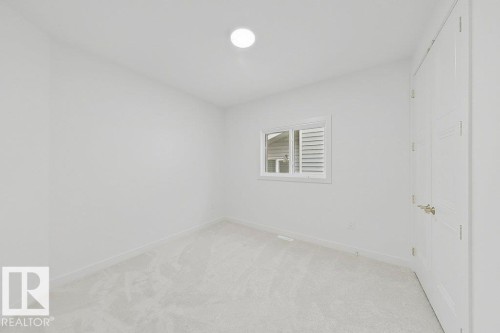 Neutral white wall paint, light-colored carpeting, white trim, a single window, and a white interior door with brushed nickel hardware - 9216 91 Street Nw, Edmonton, AB - Indoor Photo Showing Other Room