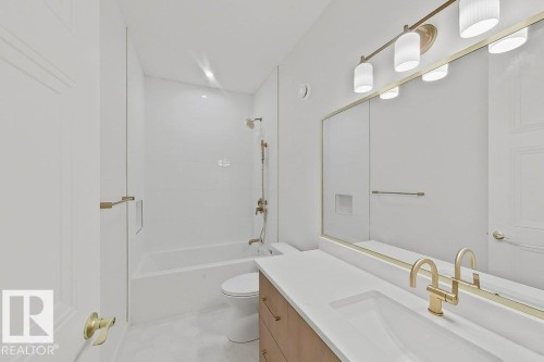 Bathroom featuring a neutral color palette, integrated sink vanity with a wood-finish base, wall-mounted mirror with brass trim, and a bathtub with white subway tile surround and brass fixtures - 9216 91 Street Nw, Edmonton, AB - Indoor Photo Showing Bathroom
