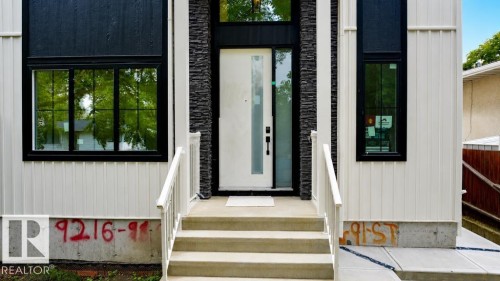 Contemporary exterior featuring vertical white siding, dark stacked stone accents, a modern entry door with sidelight, and black-framed windows - 9216 91 Street Nw, Edmonton, AB - Outdoor