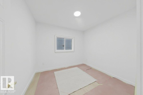 Bright interior space featuring a window with horizontal blinds, overhead lighting, and white baseboards - 9216 91 Street Nw, Edmonton, AB - Indoor Photo Showing Other Room