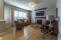 Living area featuring wood-finish flooring, a large window with blinds, and a stone-clad fireplace with a dark wood mantel - 