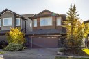 Two-story property featuring a double-bay garage, stone facade accents, multi-pane windows, and a shingled roof - 233 Hawks Ridge Boulevard Nw, Edmonton, AB 