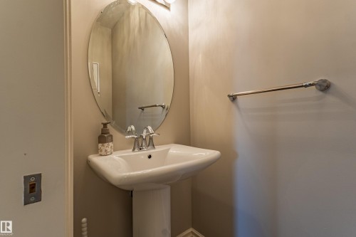 Pedestal sink with a chrome faucet, oval mirror, and wall-mounted light fixture - 233 Hawks Ridge Boulevard Nw, Edmonton, AB 