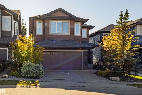 Two-story residence featuring a brown siding and stone facade, an attached double garage, and a concrete driveway - 233 Hawks Ridge Boulevard Nw, Edmonton, AB 