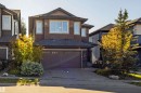 Two-story residence featuring a brown siding and stone facade, an attached double garage, and a concrete driveway - 233 Hawks Ridge Boulevard Nw, Edmonton, AB 