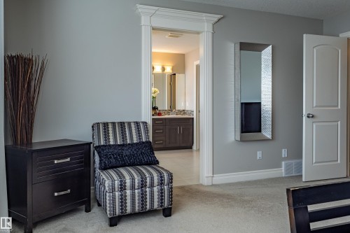 Cased doorway with decorative trim, leading to a bathroom featuring a vanity with dual sinks, wall-mounted light fixtures, and a framed mirror - 233 Hawks Ridge Boulevard Nw, Edmonton, AB 