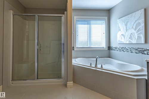 Built-in corner bathtub with deck-mounted fixtures, adjacent to a window with blinds, and a glass-enclosed shower with sliding doors - 233 Hawks Ridge Boulevard Nw, Edmonton, AB 