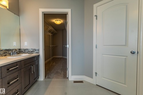 Vanity with a single basin sink, mosaic tile backsplash, and dark wood-finish cabinetry - 233 Hawks Ridge Boulevard Nw, Edmonton, AB 