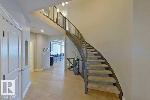 Curved staircase with metal balusters, wood-finish flooring, arched doorway, and recessed ceiling lighting - 233 Hawks Ridge Boulevard Nw, Edmonton, AB 